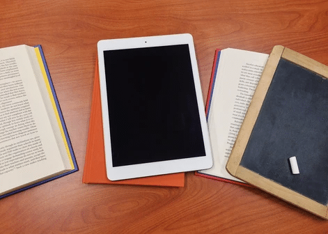 Books on table opened next to a tablet.